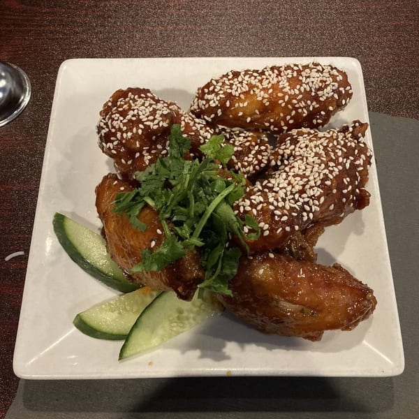 Sizzling Kitchen's Asian-fusion chicken wings, glazed with sesame seeds, cilantro, and cucumber slices.