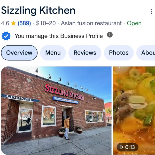 Exterior of Sizzling Kitchen, a brick building with a red sign, and a person walking towards the entrance.
