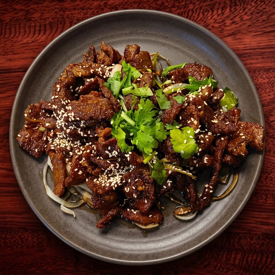 A dark plate of sesame beef with cilantro and onions on a dark wooden table.