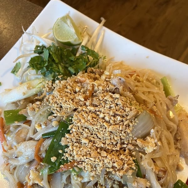 Sizzling Kitchen's Pad Thai with noodles, chicken, peanuts, lime, and cilantro on a white plate.