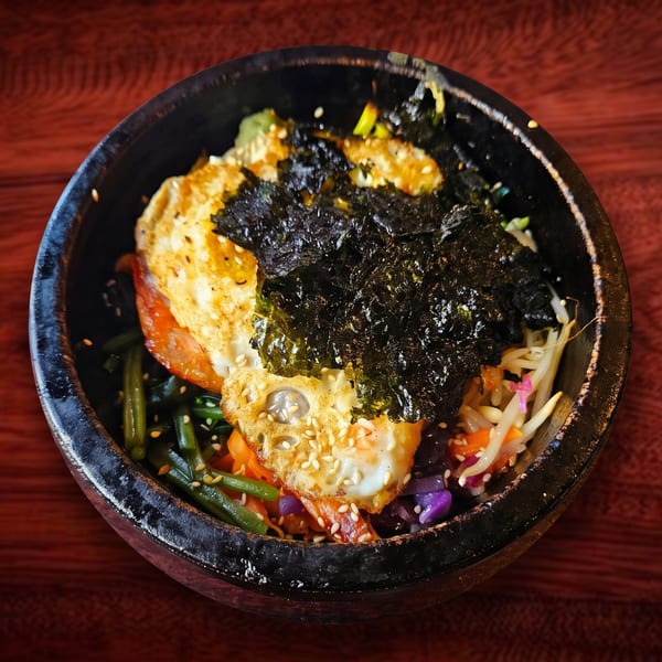 Bibimbap in a black stone bowl, topped with a fried egg, seaweed, and sesame seeds.
